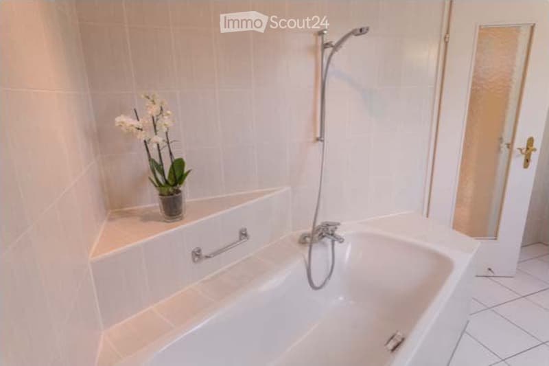 Modern bathroom with a white bathtub, a handheld showerhead, a chrome faucet, and a small flower vase on the edge of the tub.