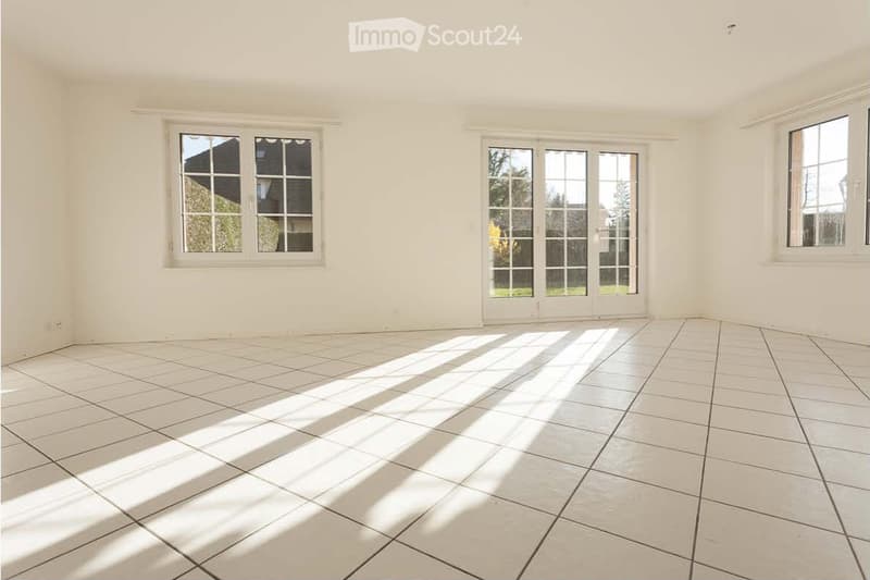 Empty room with white tiled flooring and large windows allowing natural light to enter. The space is unfurnished, showing only the basic structure of the room.