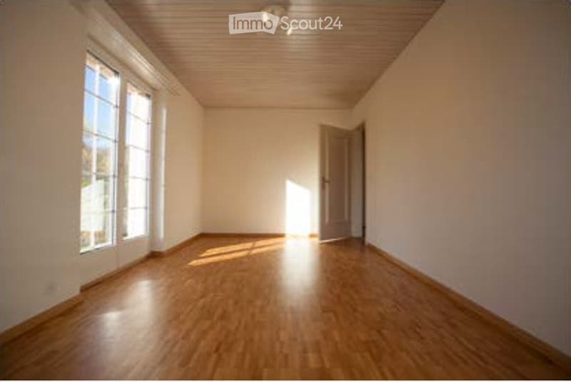 Empty room with wooden flooring, white walls, large windows, and a door.