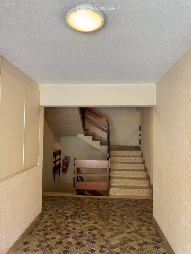 Hallway with a staircase leading upwards, beige walls, patterned tile floor, and a round ceiling light fixture.