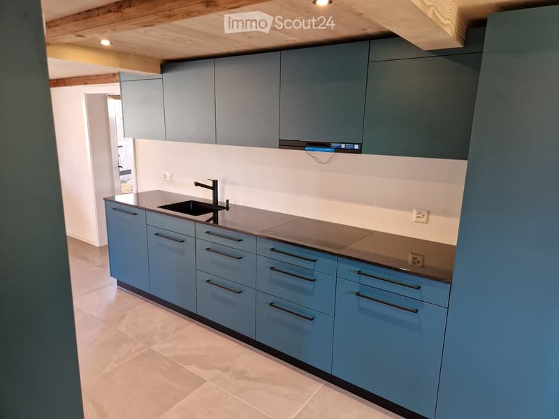 Modern kitchen with light blue cabinets, stainless steel sink, and stove. Exposed wooden ceiling beams and tiled floor.
