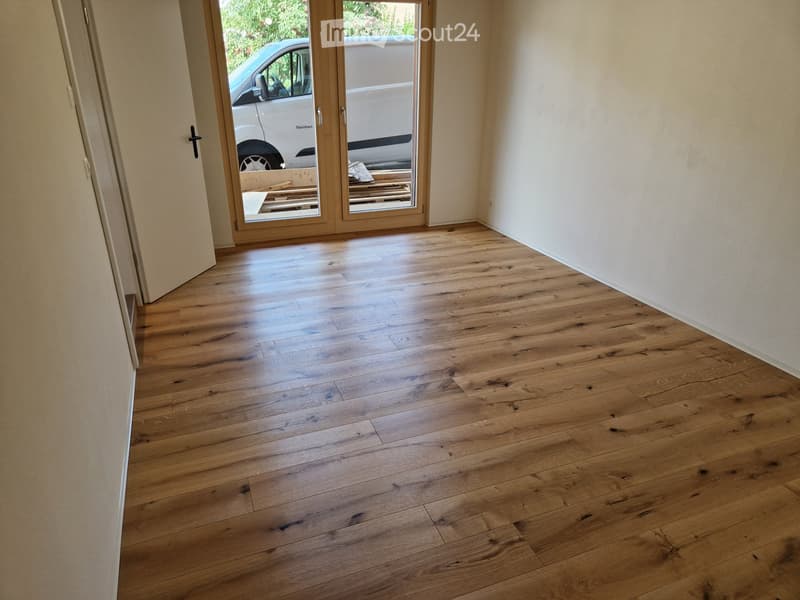 Empty room with light wooden flooring and white walls, featuring a sliding glass door leading outside.