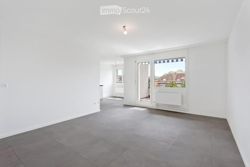 Completely empty room with white walls, grey tiled floor, and large sliding glass doors leading to a balcony.