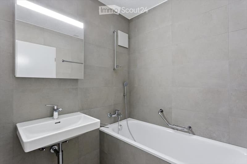 Modern bathroom with a white sink, bathtub, large mirror, and sleek fixtures.