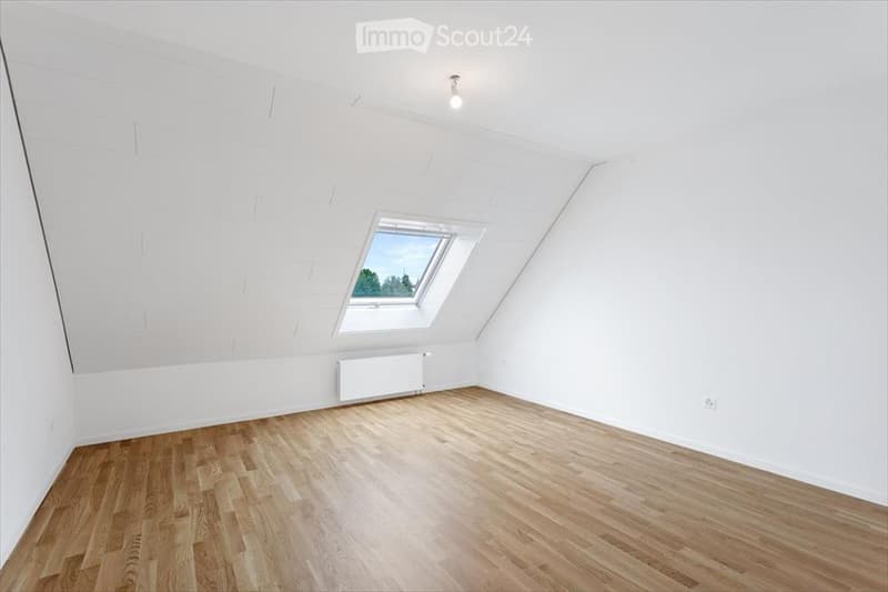 Completely empty attic room with wooden flooring, white walls, and a skylight window.