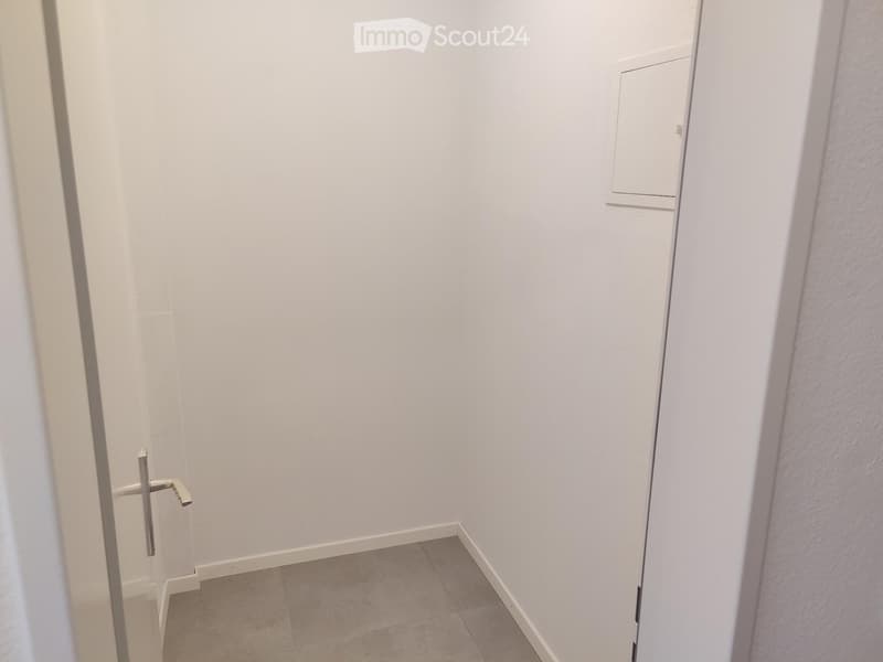 Empty hallway with white walls, tiled floor, and a closed door on the left side.