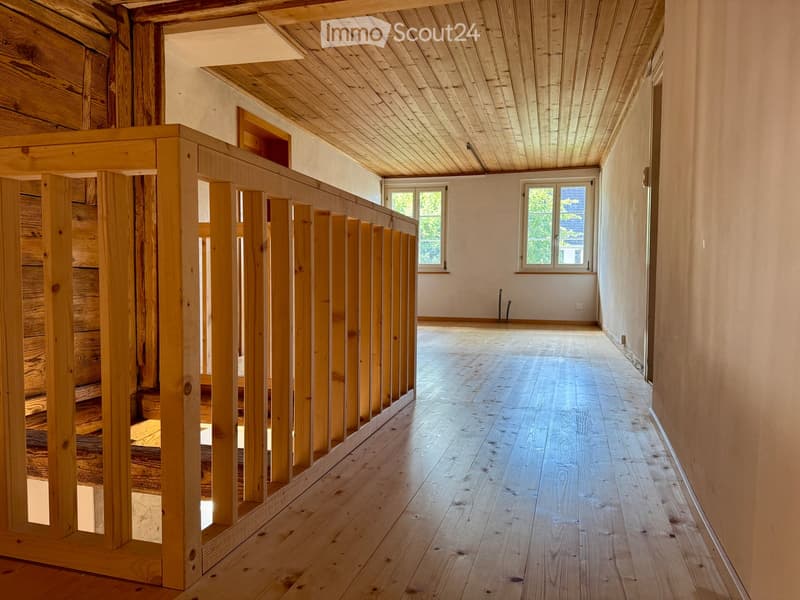 Empty wooden staircase leading to an open space with wooden floors and white walls, featuring two windows at the far end.
