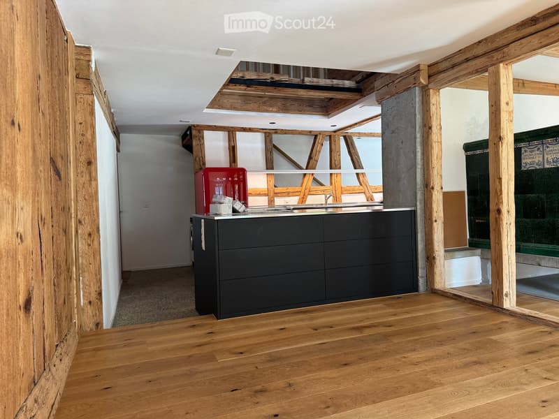 Modern kitchen with wooden floors, exposed wooden beams, and a black cabinet. A red refrigerator is placed on the counter.