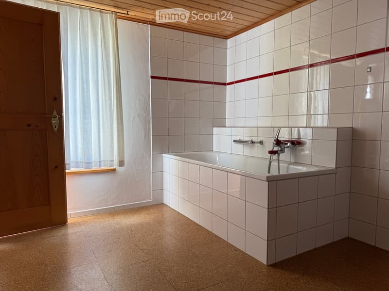Bathroom with a white tiled wall, a bathtub, and a wooden door with a curtain.