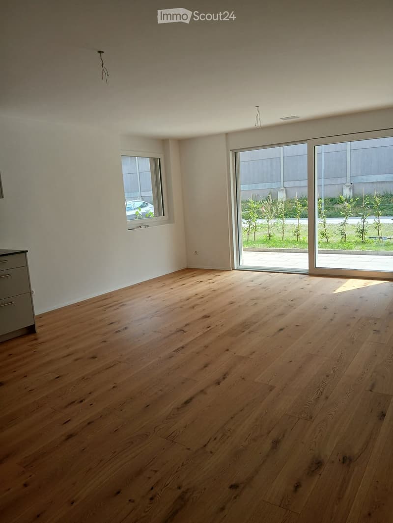 Empty room with light wooden flooring, white walls, large sliding glass doors leading to an outdoor area, and a small window on the left side.
