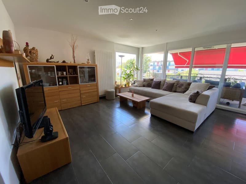 Modern living room with dark tiled floor, large sectional sofa, coffee table, TV stand, wooden cabinet, and decorative items on shelves.