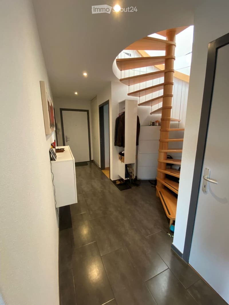Modern hallway with dark tiled floor, white walls, built-in storage unit, and a wooden spiral staircase leading to an upper level.