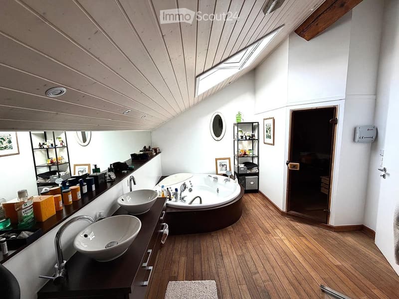 Modern bathroom with wooden flooring, double sinks, a large bathtub, and shelves holding toiletries and decorative items.