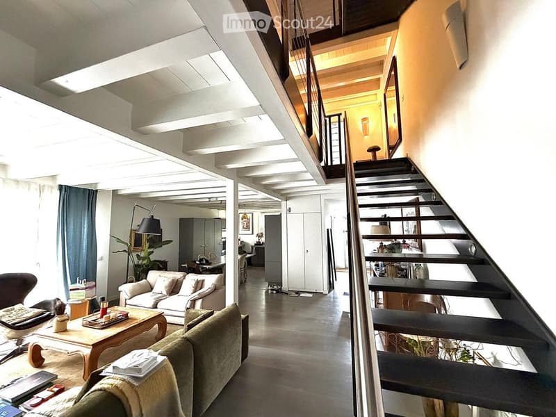 Open-plan living area with a staircase leading to an upper level, featuring a sofa, coffee table, chair, and decorative items.
