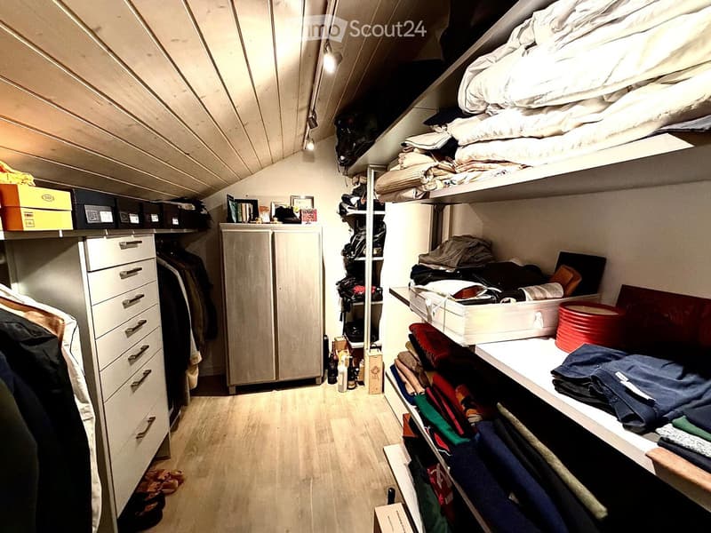 Well-organized walk-in closet with built-in wardrobe, shelves, and drawers. Contains neatly arranged clothing, bedding, shoes, and storage boxes.