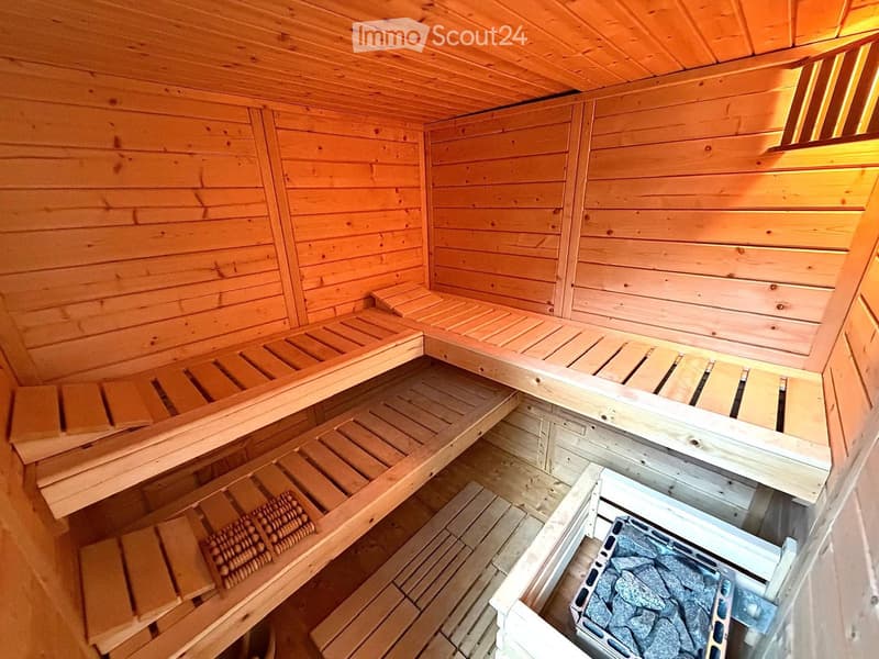 Wooden sauna interior with multiple wooden benches and slats, stone heater in the corner.