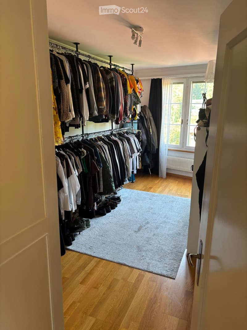 Spacious walk-in closet with wooden flooring, large clothing rack, shoe rack, and a grey rug in the center.