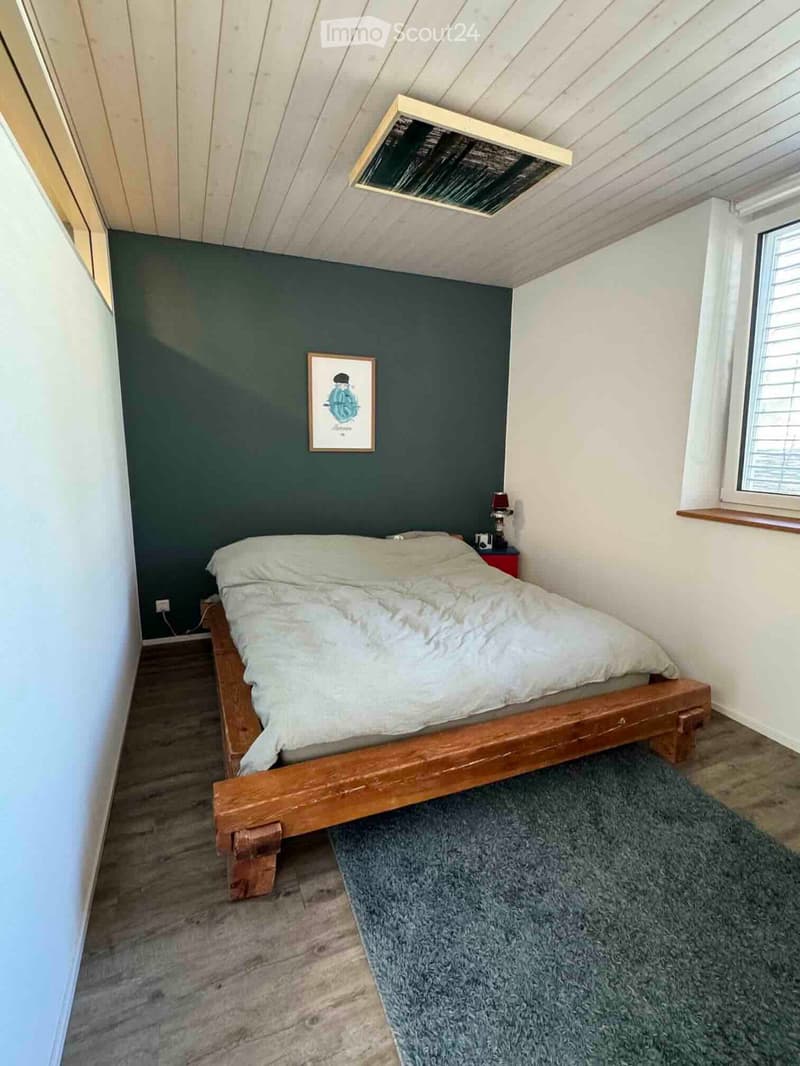 Cozy bedroom with wooden bed, nightstand, lamp, picture frame, and a gray rug on wooden floor.