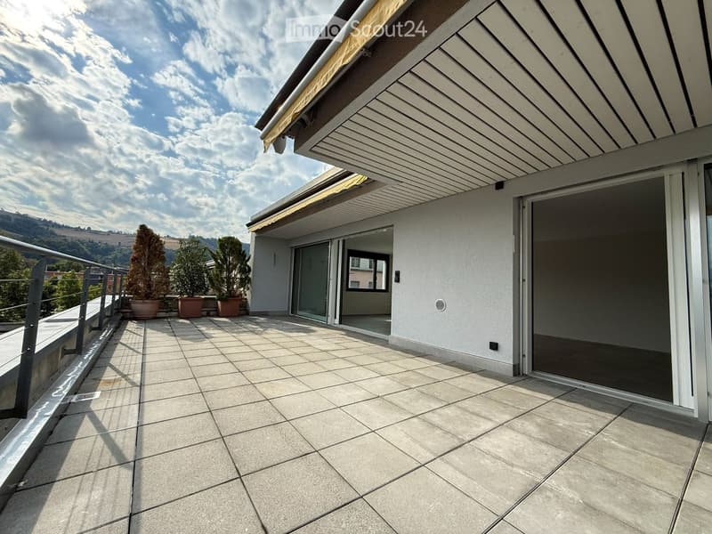 Modern balcony with tiled flooring, glass sliding doors, and potted plants, offering a scenic view of the surrounding landscape.