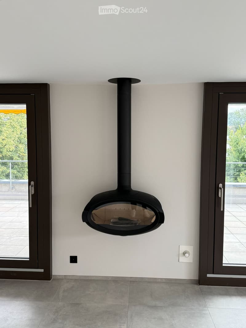 Modern room with a sleek black fireplace mounted on a white wall, flanked by two large sliding glass doors leading to a balcony or outdoor area.