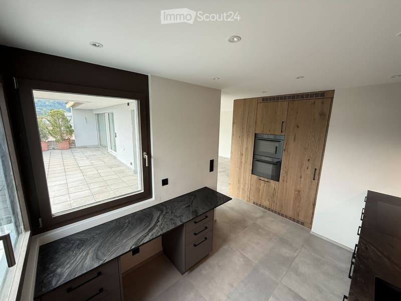Modern kitchen with wooden cabinets, marble countertop, and built-in oven. Large window offers a view of the outdoor area.