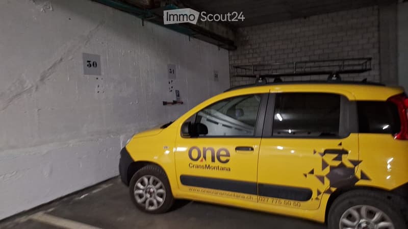 Underground parking area with a yellow car parked inside, featuring exposed brick walls and numbered parking spots.