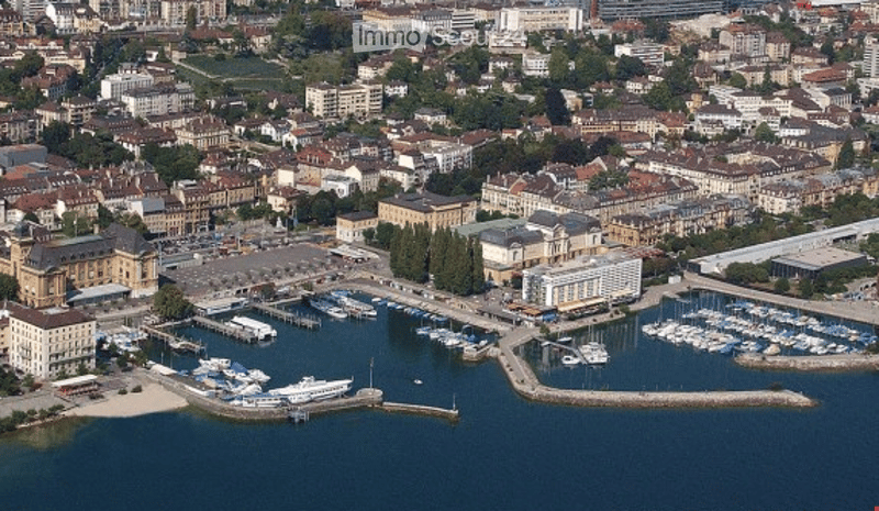 Aerial view of a cityscape with a waterfront featuring a marina with numerous docked boats, surrounded by buildings and structures.