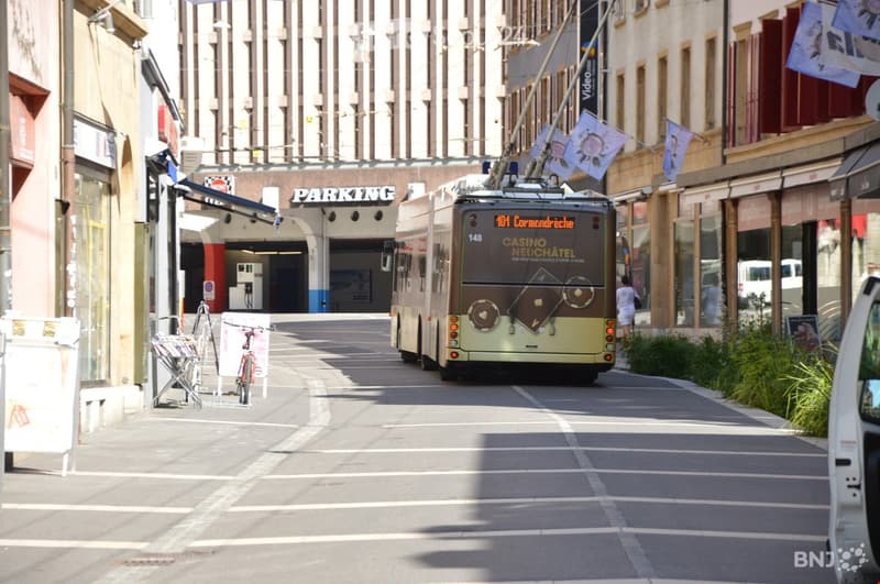 A city street lined with buildings, featuring a tram, bicycles, and a parking sign.