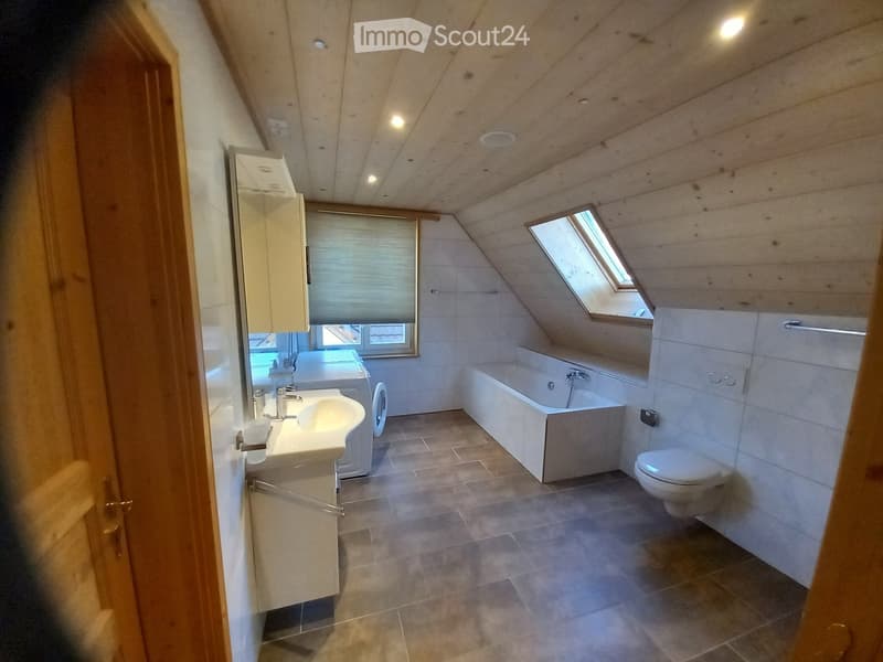 Modern bathroom with a sloped wooden ceiling, skylight window, tiled floor, and white fixtures including a sink, bathtub, toilet, and mirror.