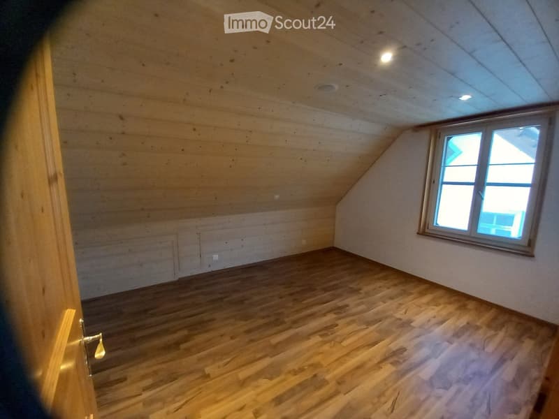 Empty attic room with wooden floors, exposed wooden beams, and a single window letting in natural light.