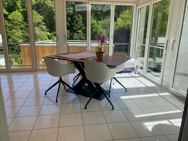 Bright dining area with large glass doors leading to a balcony, featuring a modern wooden table, white chairs, and a flower pot on the table.