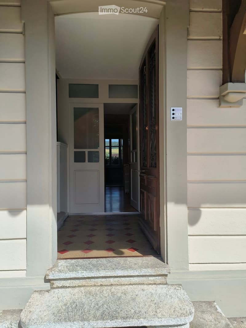 Entrance hallway with tiled floor, double doors leading to another room, and a view of a garden through the open door.