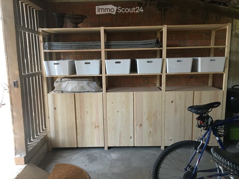 A wooden shelving unit with multiple compartments and storage bins, a bicycle, and a fan in a garage-like space.