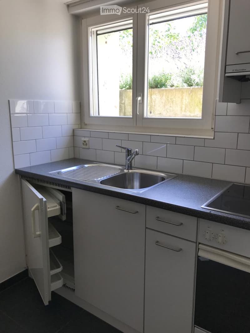 Modern kitchen with white tiled walls, stainless steel sink, grey cabinets, and built-in oven.