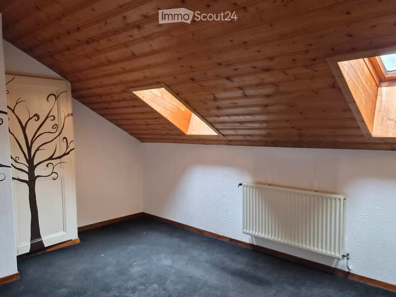 Empty room with wooden slatted ceiling, skylight windows, grey carpet, white walls, and a radiator.