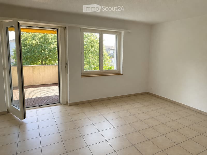 Empty room with tiled floor, white walls, large window, and sliding glass door leading to a balcony.