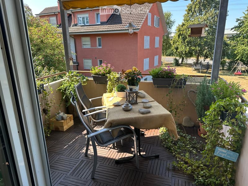 Balcony with wooden decking, table with chairs, flower pots, and decorative items.