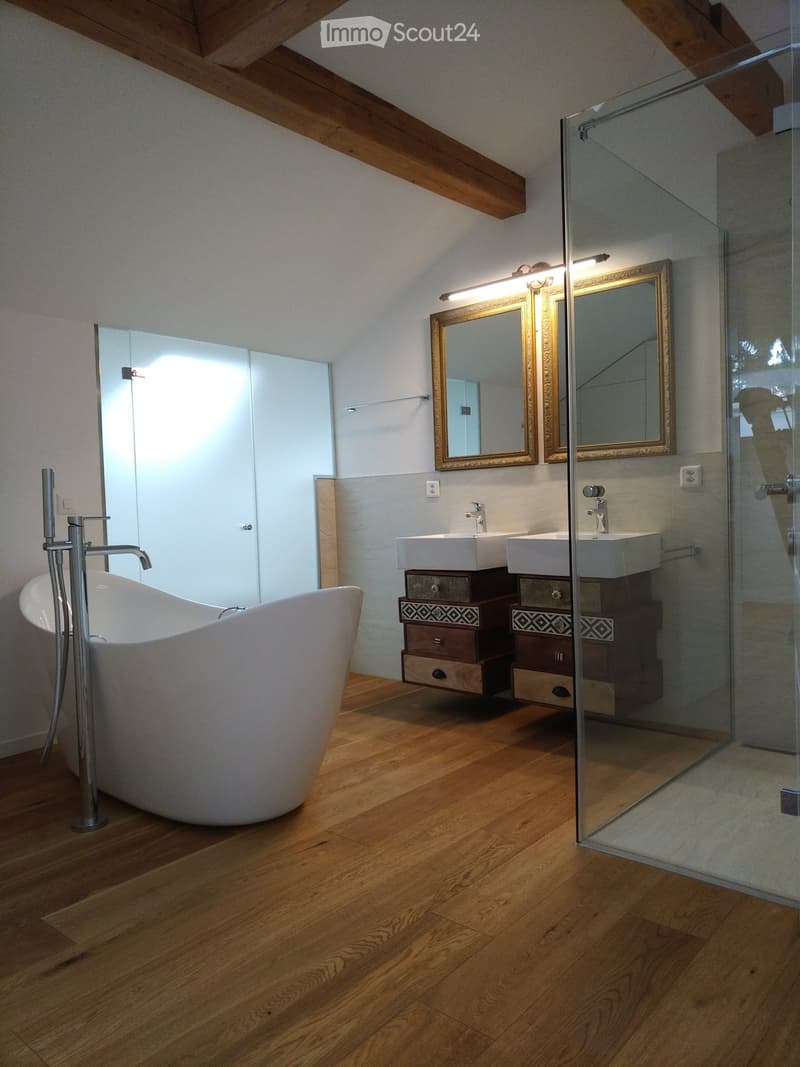 Modern bathroom with wooden flooring, a freestanding bathtub, double sink vanity with mirrored cabinets, and a glass-enclosed shower area.