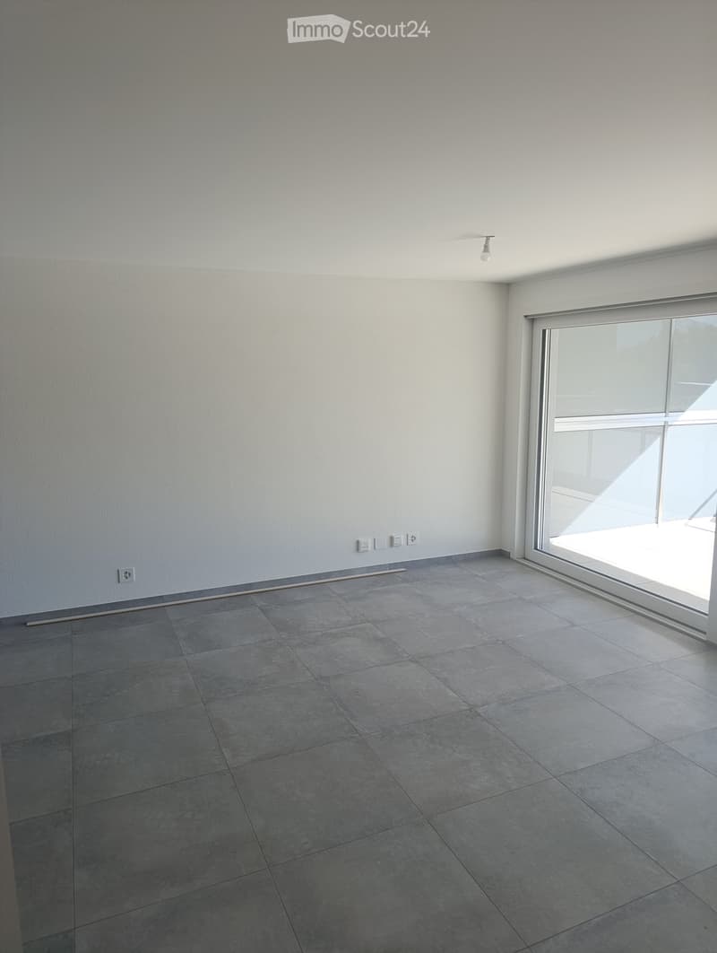 Empty room with grey tiled floor, white walls, large window, and electrical outlets.
