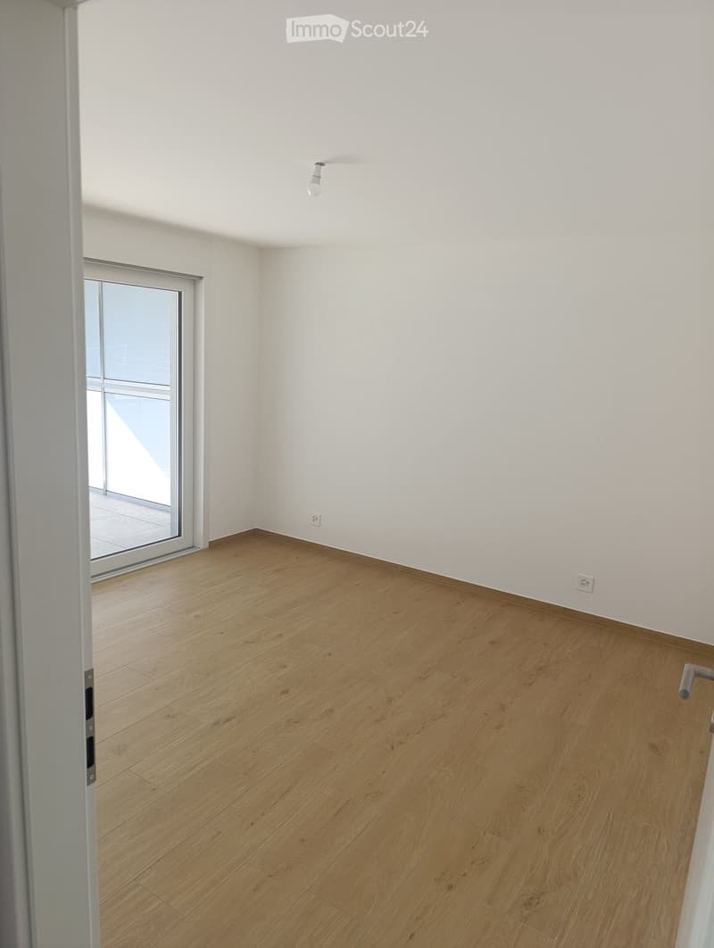 Empty room with light wooden flooring, white walls, and a sliding glass door leading to a balcony.