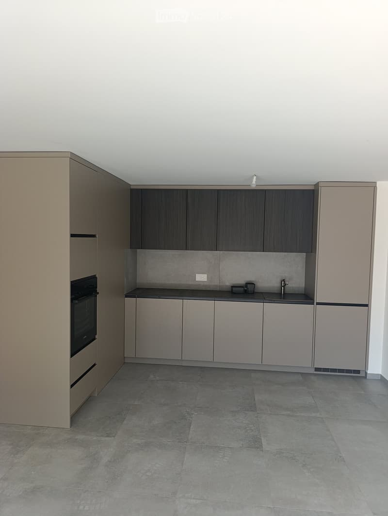 Modern kitchen with grey cabinets, dark countertops, and tiled floor. Features an oven on the left and a sink with a faucet on the right.