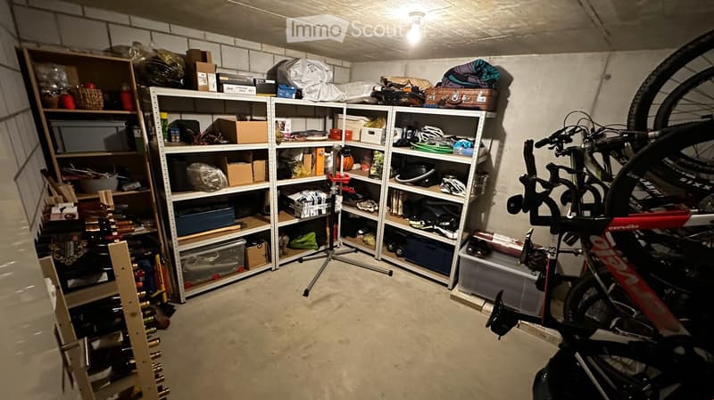 A well-organized garage with metal shelving units filled with various items, including storage boxes, tools, and bicycles. The space features concrete flooring and exposed brick walls.