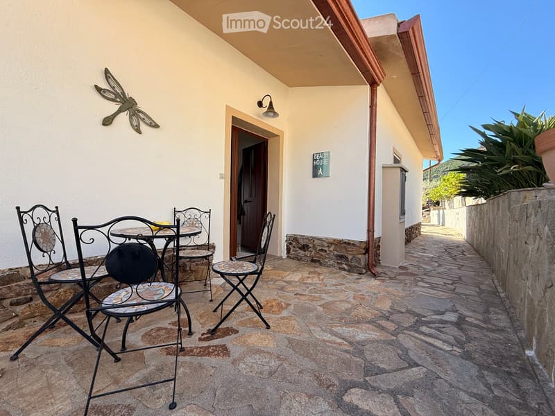 Balcony with stone flooring, metal table and chairs, decorative wall art, and a sign reading "BEACH HOUSE".