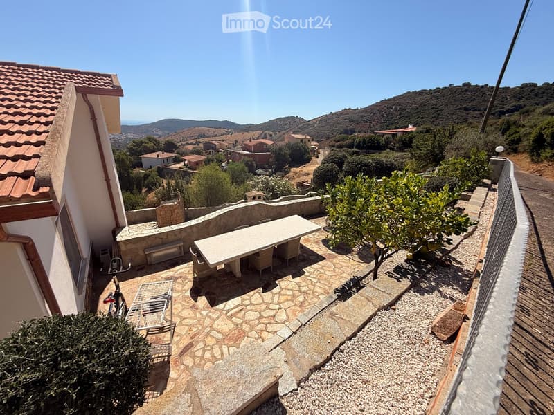Terrace with stone flooring, outdoor table and chairs, bench, bicycle, and lounge chair, overlooking a scenic countryside view.