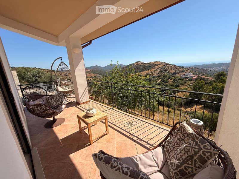 Balcony with wicker chairs, small table, and scenic mountain view.