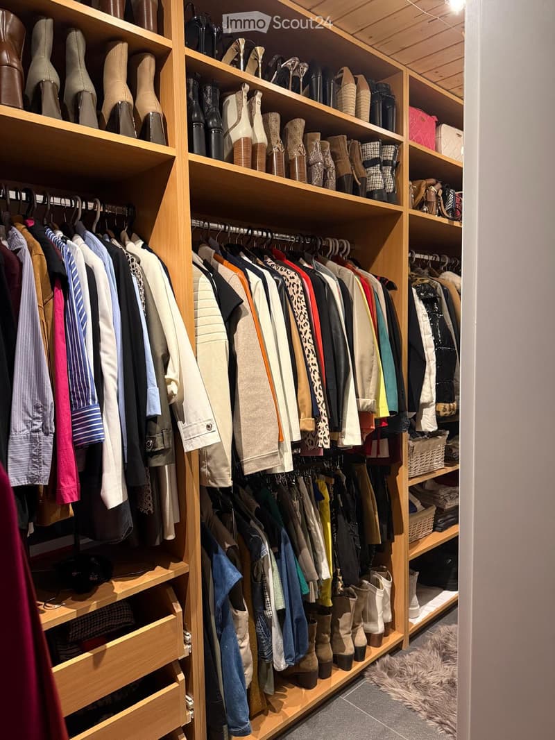 A well-organized walk-in closet with wooden shelves and hanging rods, filled with neatly arranged clothing, shoes, and accessories.