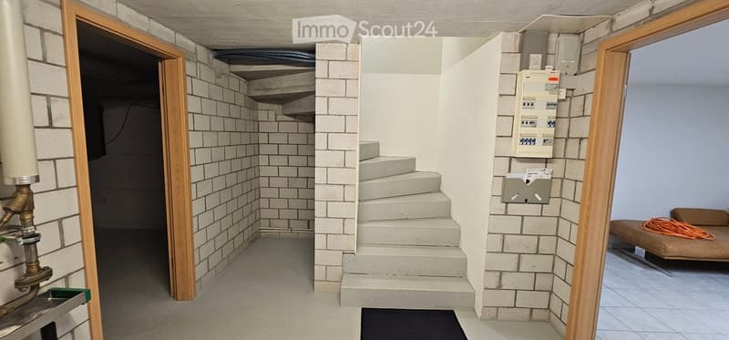 Empty utility room with brick walls, concrete steps leading up, electrical panel, water heater, and a small bench with an orange extension cord.