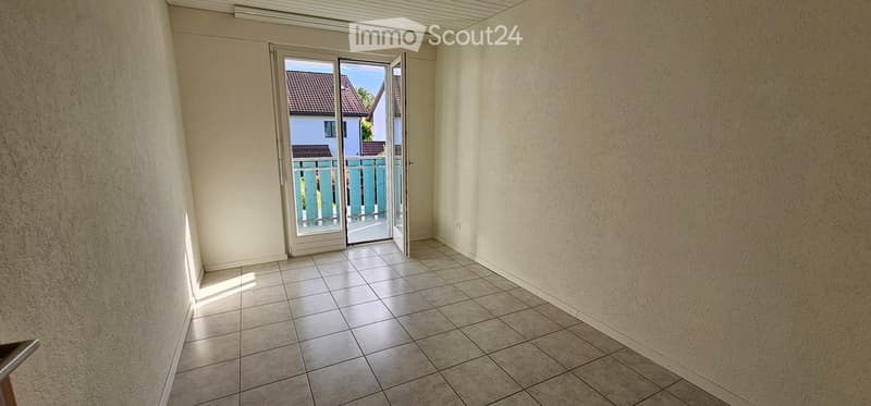 Empty room with tiled floor, white walls, and a sliding glass door leading to a balcony or outdoor area.