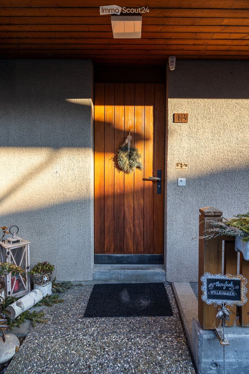 wooden door, concrete wall, welcome sign, small plants, gravel path