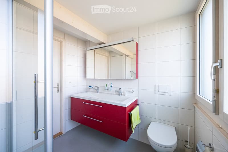 Bathroom with white tiles, red vanity, white sink, mirror, shower, toilet, and window